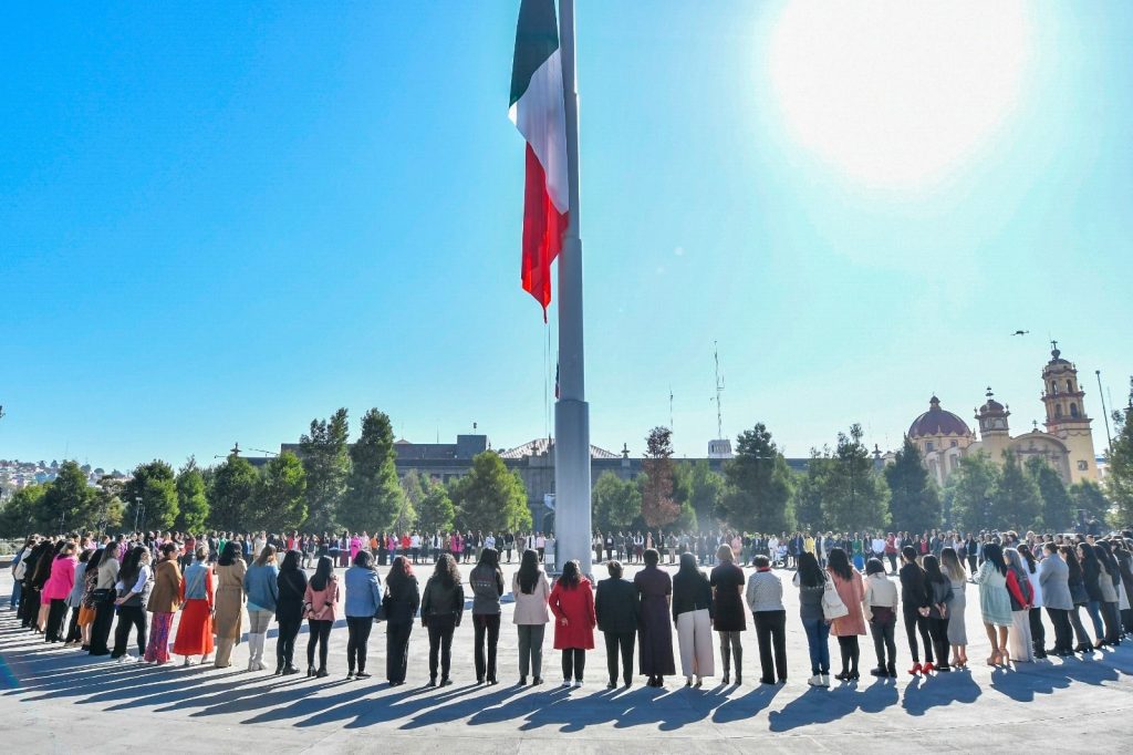 Acto conmemorativo del Día Internacional de las Mujeres en Toluca con decenas de mujeres reunidas alrededor del asta bandera.